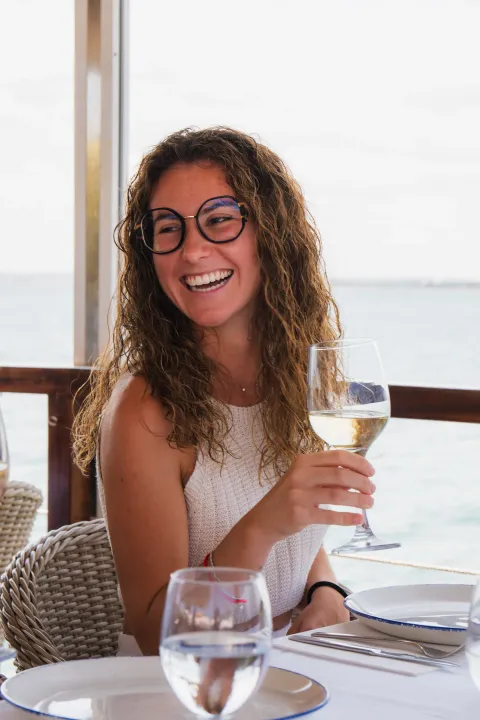 Clienta sonriendo con una copa de vino blanco en la terraza